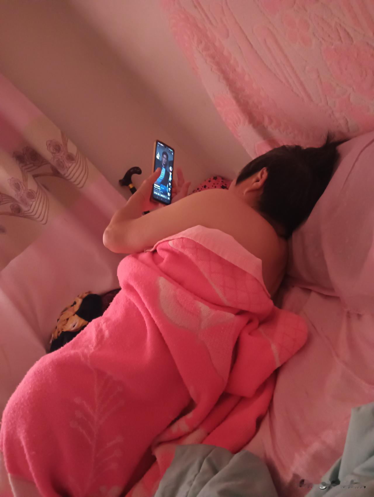 这个人裹着毯子在床上玩手机。