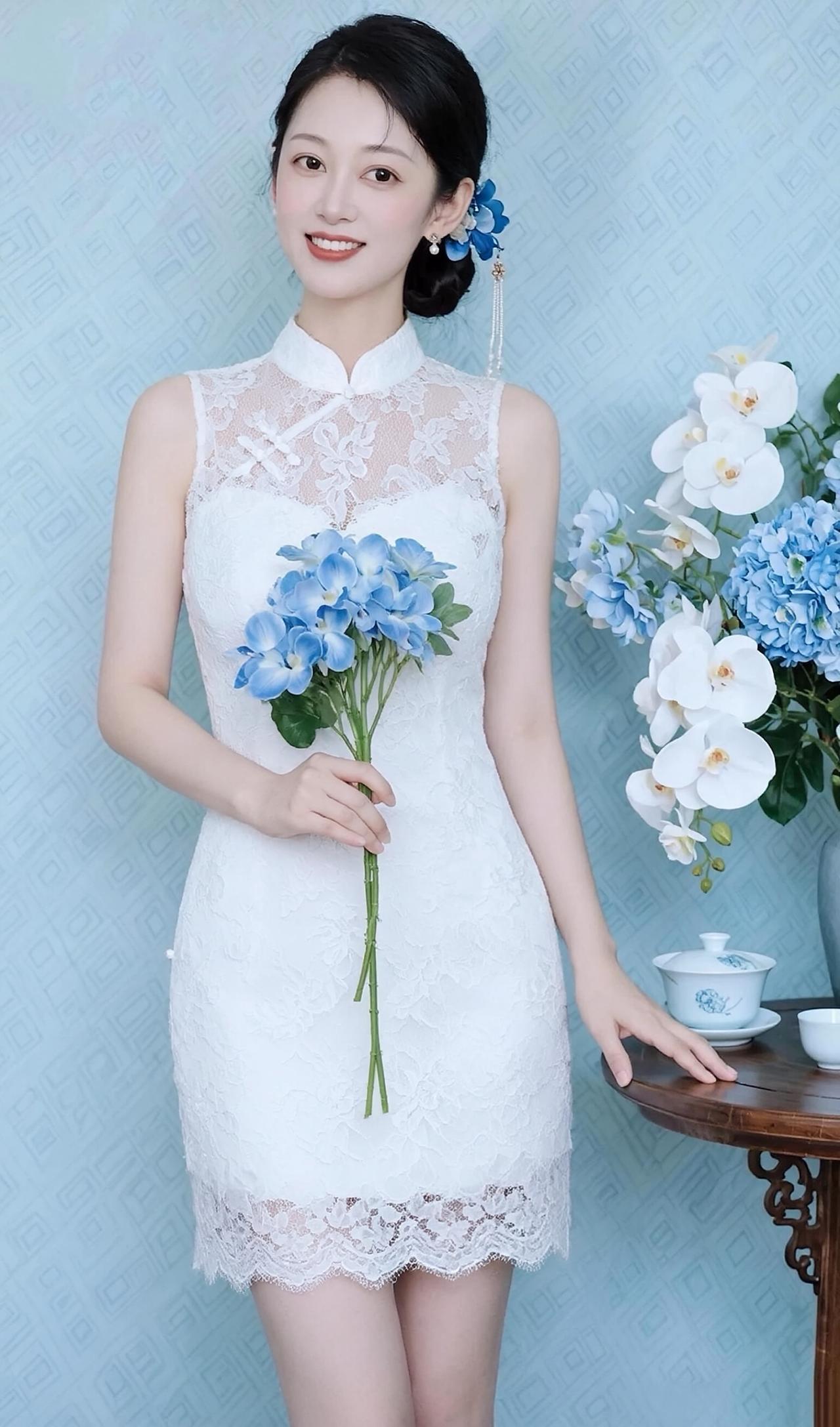 她眉眼弯弯，笑容温柔明媚，乌黑秀发盘起，鬓边点缀着蓝色花饰与垂坠流苏，精致又灵动