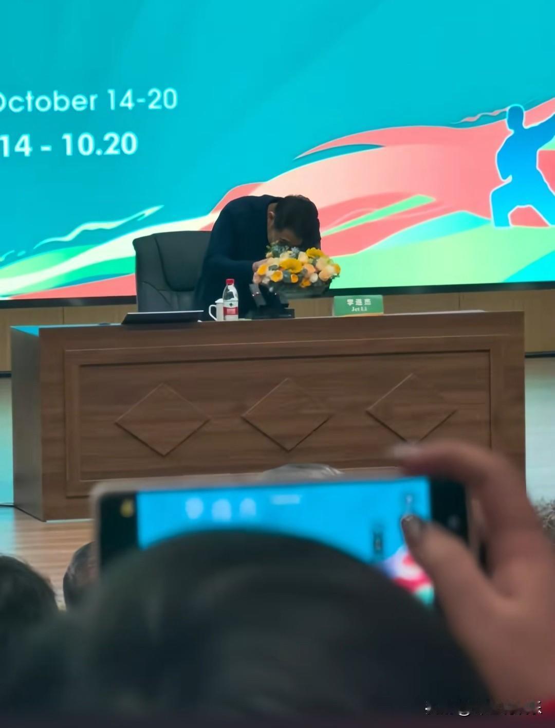 李连杰上台准备发言，看到桌上的黄色花束，弯腰小心翼翼挪到旁边，这一动作暴露了文化