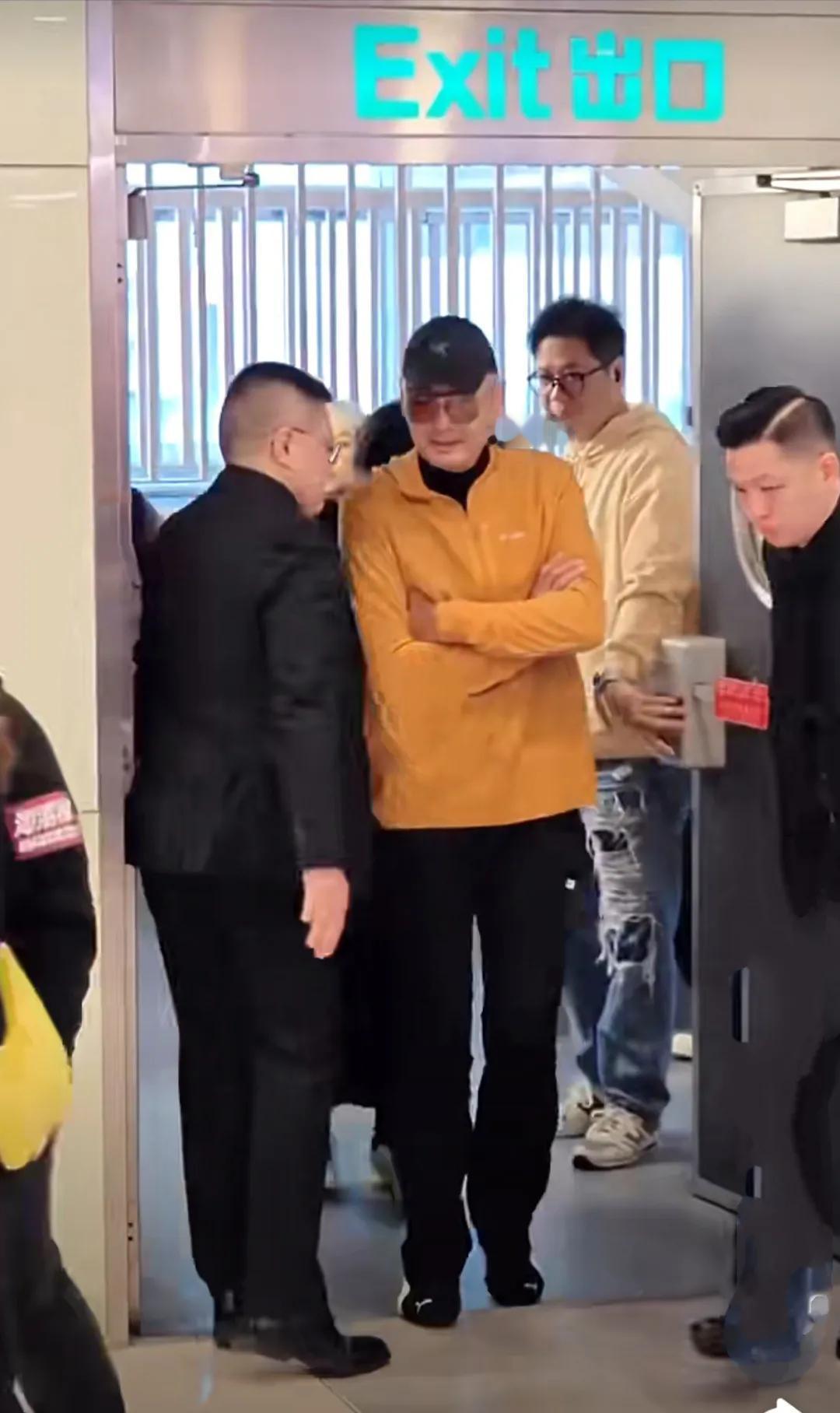 周润发在海城港举办慈善摄影展，一身黄色上衣外套，配黑色长裤皮鞋，戴着眼镜，头上棒