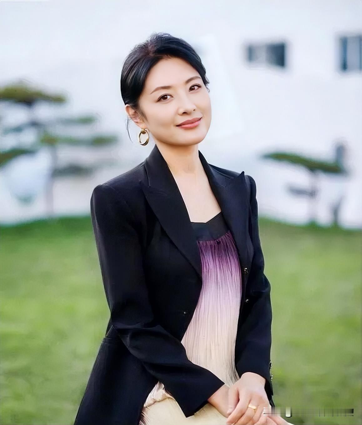 微风拂过青草地，她静坐如诗。黑色西装交织温柔裙摆，耳畔金环轻摇。眉眼间的笑意，是