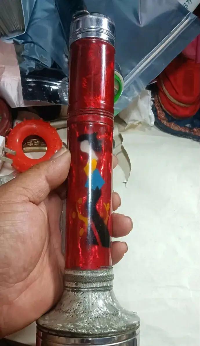手拿红色塑料玩具，背景杂物堆。用家乡话这个叫什么？属于家用电器吗？[捂脸]