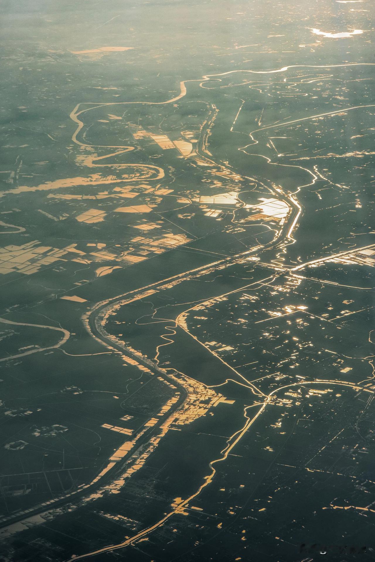 翻出一张多年前在飞机航班上拍摄的照片，大地上的河流和水田像破碎的镜面一样反射着夕