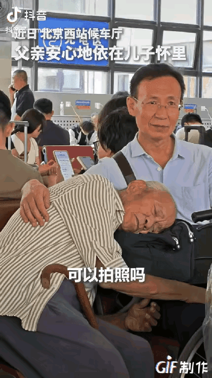 在候车厅里，老父亲累了，把头倚在了儿子的腿上，儿子乐呵呵的用手扶着父亲的身体，当