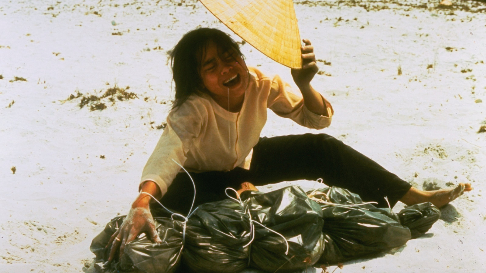 1969 年 4 月，在古城顺化附近，一位年轻的南越女子跪在沙地上，她身前的塑料