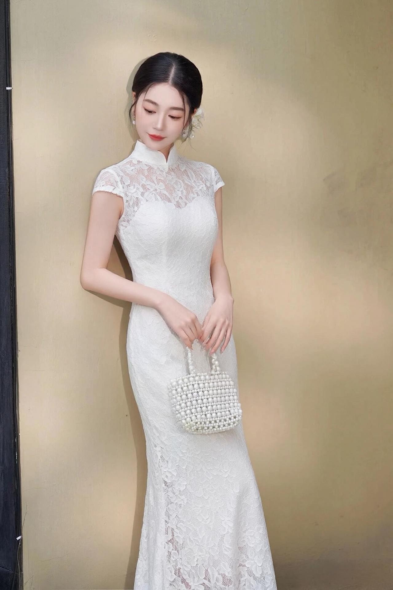 她身姿窈窕，旗袍采用精致的镂空蕾丝面料，高领设计勾勒出修长的天鹅颈，无袖剪裁露出