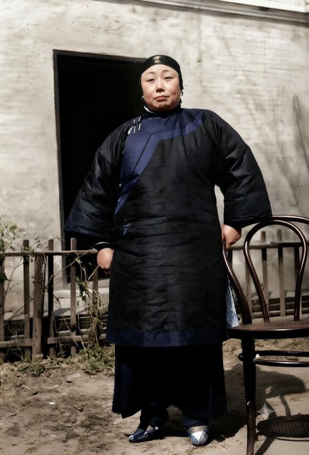 1940年，江苏，一地主婆面相富态，身穿黑色绸缎斜襟长棉袍，头戴抹额，脚踩传统布