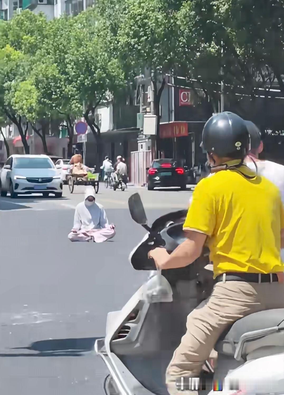 近日，在广东发生了一起惊险的一幕。

只见一名女子盘腿坐在马路中间，来往的车辆不