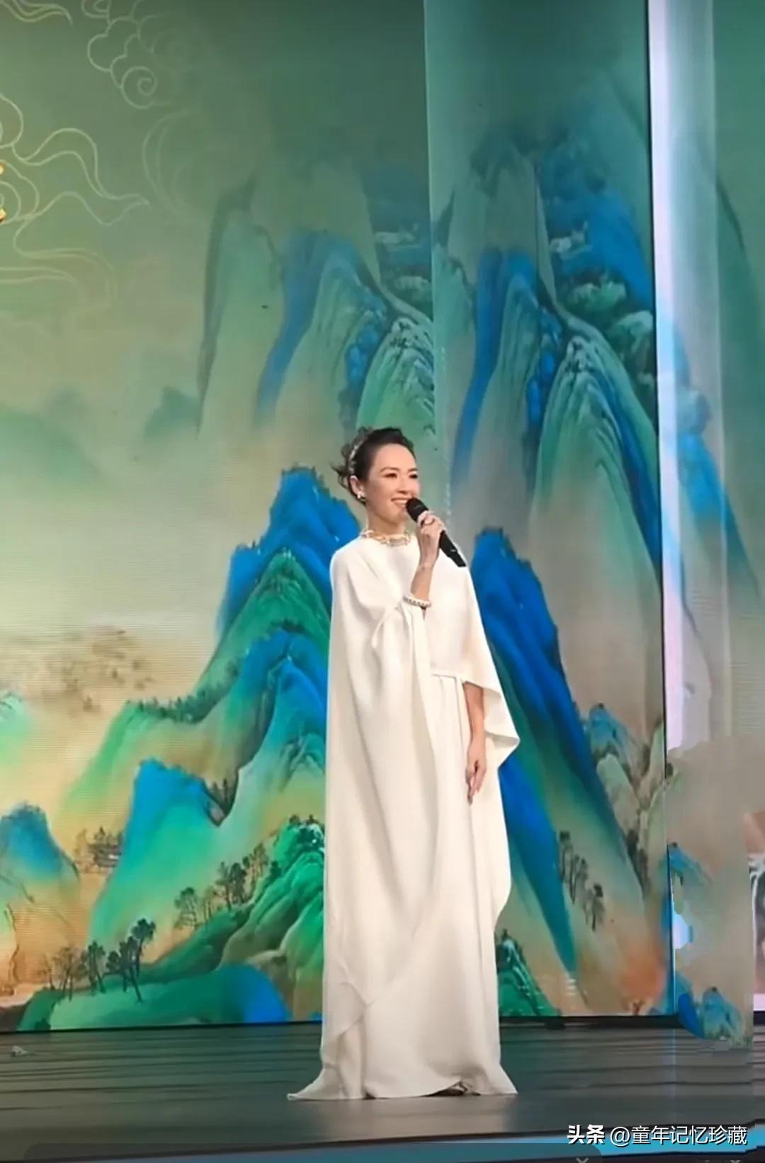 章子怡一身米白色蝙蝠衫亮相上合组织国家电影节，舞台上背景是中国风山水画，章子怡走