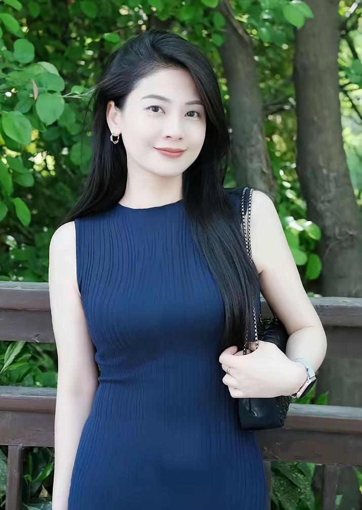 一袭深蓝无袖修身裙，勾勒出优雅身姿，耳畔金饰轻晃，手挽黑色链条包，于葱郁绿意间，