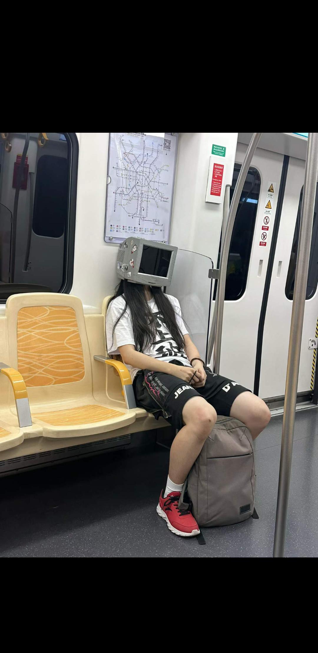 成都地铁上，一名乘客戴着两个红色水桶改造的头盔，上面还装了类似摄像头的装置，看起