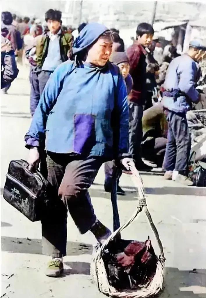 1988年，山东临沂大集上，一个正在售卖大公鸡的老大娘，这张老照片里的农村妇女，