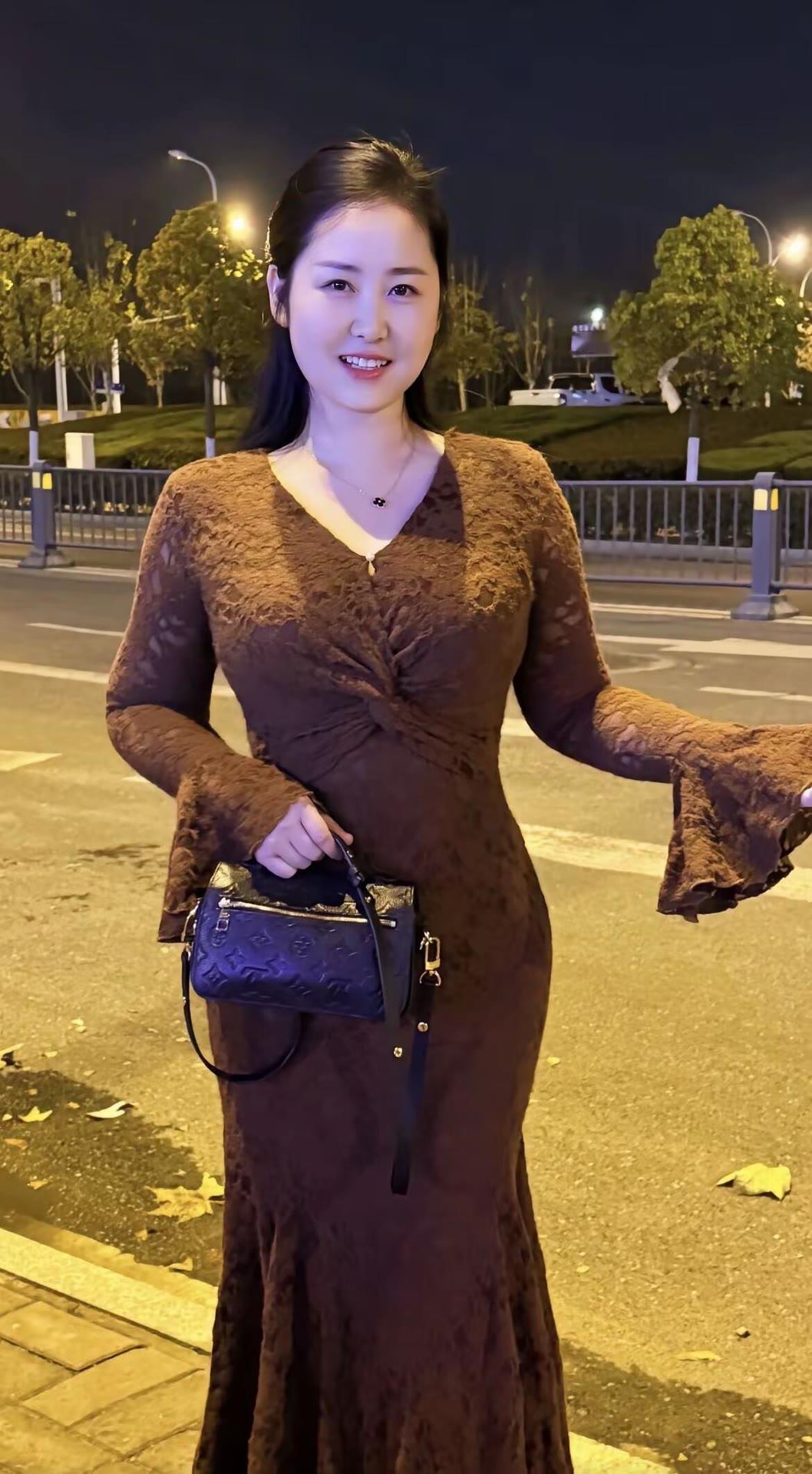 夜晚街拍，优雅棕色长裙，手拿时尚包包，微笑面对镜头。