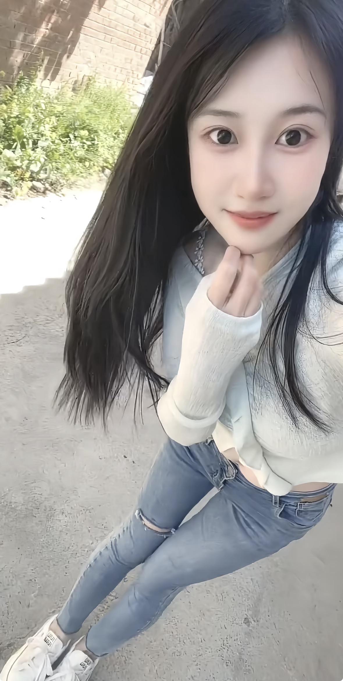 一位年轻女子坐在舒适的米色沙发上，低头专注地看着手中的手机。她身穿白色无袖Pol