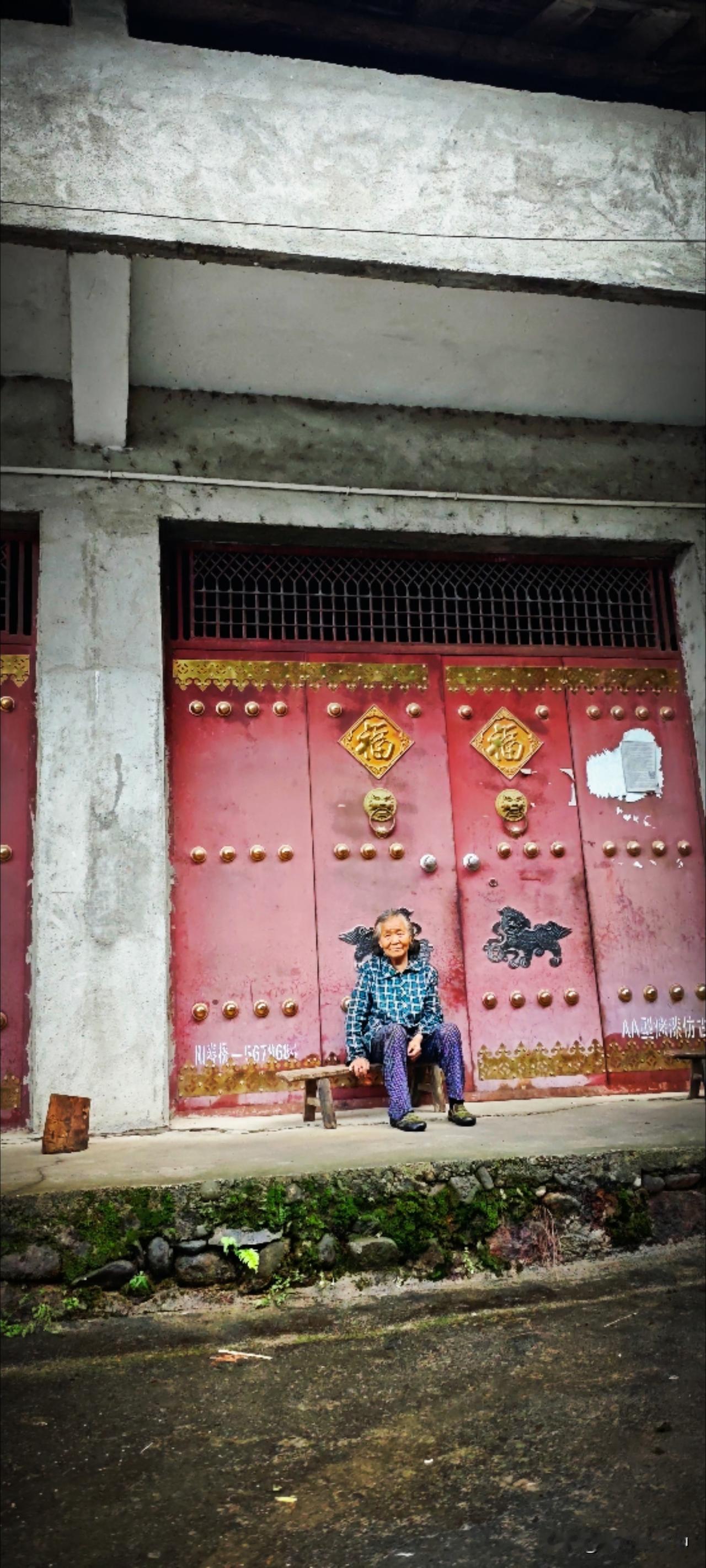 紧闭的大铁门前，老人坐在板凳上，模样温婉，安静消夏。人老了，经历过了，看透过了，