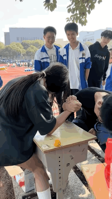 男女生在上体育课的闲暇时间进行了掰手腕较量，书桌放到空地上，男女生的胳膊肘放在桌