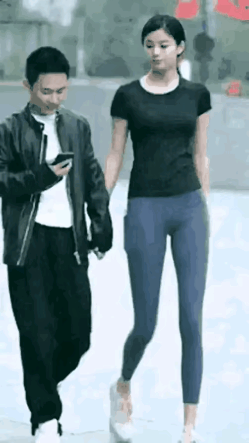 街头一对女高男矮情侣散步，男友低头拿着手机看，女友被男友冷落，转身一副撒娇的样子