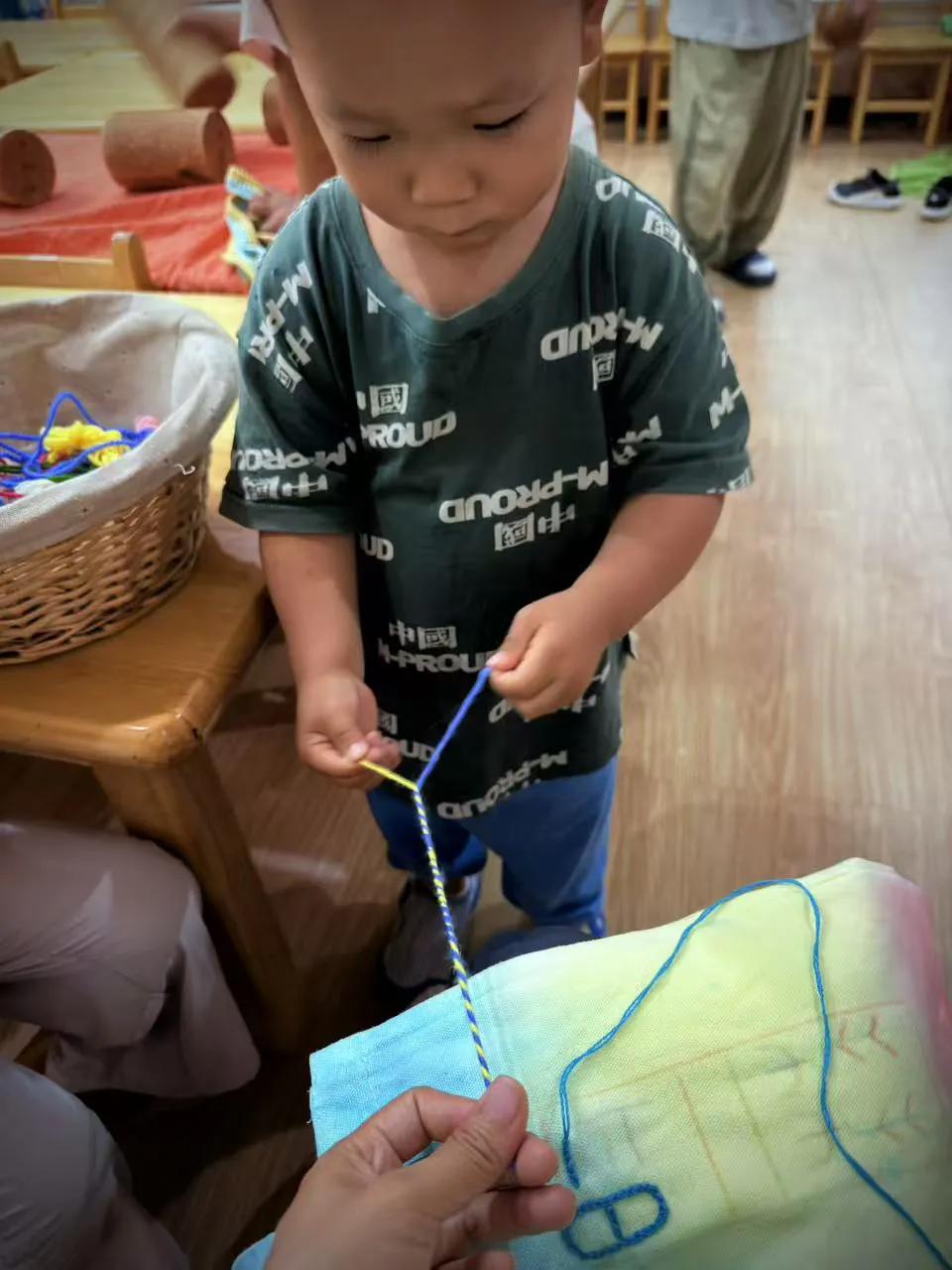 手工课上，小朋友们围坐在一起搓彩绳。五颜六色的棉线摆在桌上，老师先示范把两根线捏