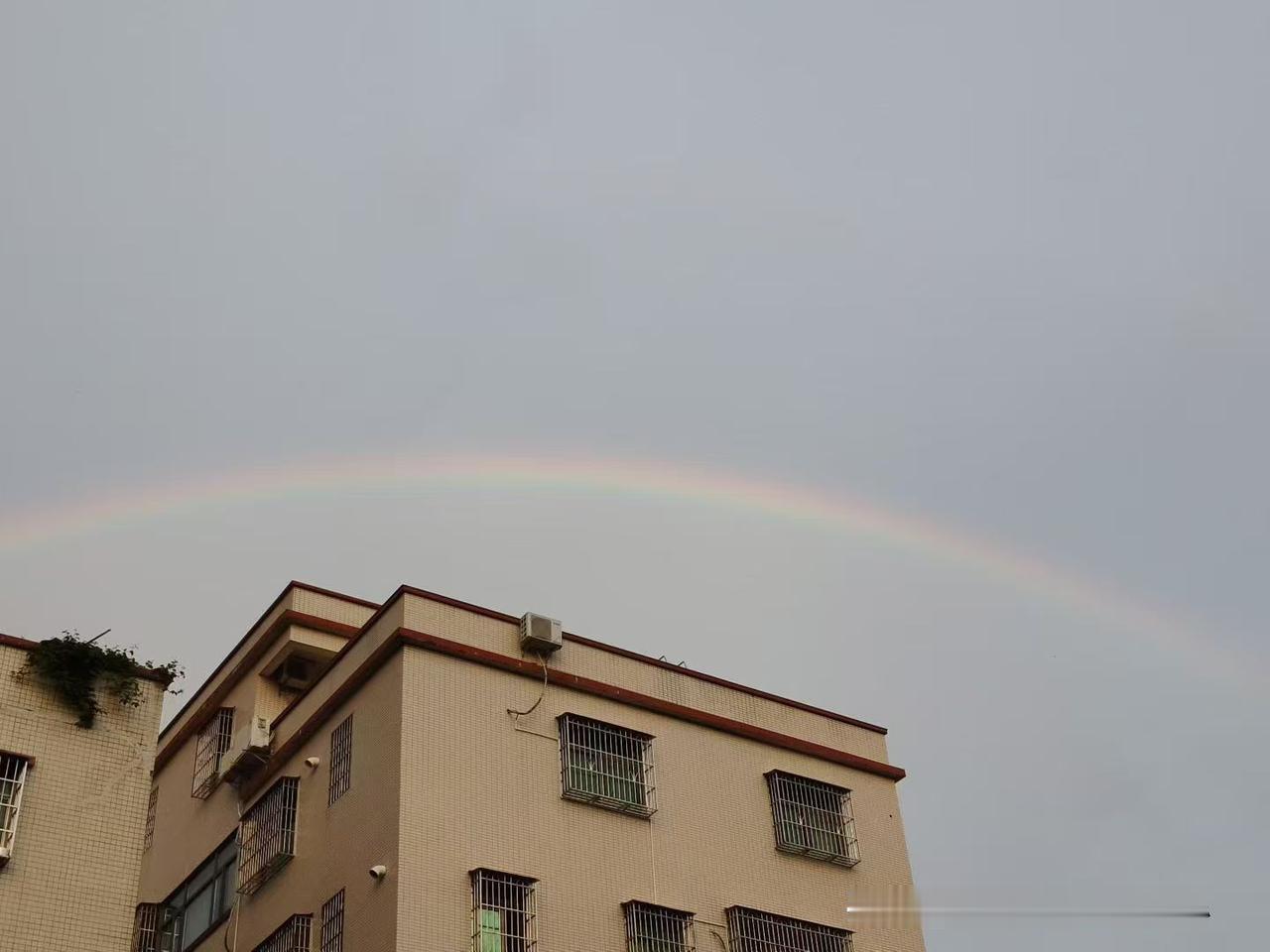 一场夏雨过后，意外邂逅了悬在楼房上空的一道淡淡的彩虹。
灰蒙蒙的天空褪去燥热，温