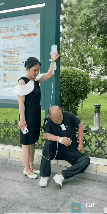 男子生病到医院打吊瓶，烟瘾上来了，病房内不能抽烟，让媳妇手举吊瓶到室外树荫下抽烟