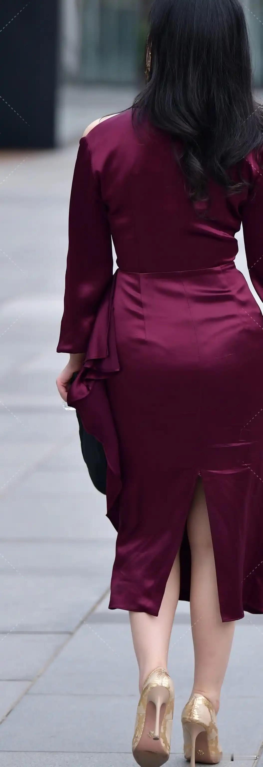 这位女士穿着红色连衣裙，搭配金色高跟鞋，走在街上。