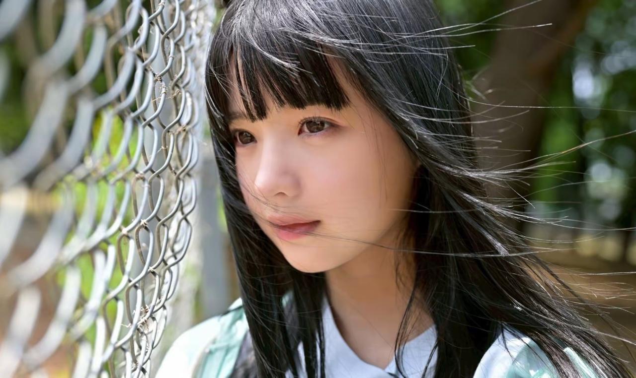 风把发丝吹得轻扬，靠在金属网边，让夏日的绿意与细碎的情绪，都融进这帧温柔的瞬间里