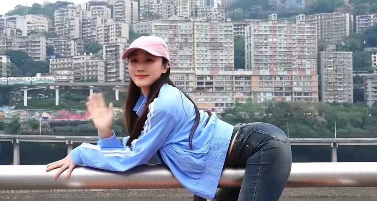 一位头戴粉色帽子、身穿蓝色上衣的女子正倚靠在栏杆上，摆出凸显曲线的姿势；而在其身