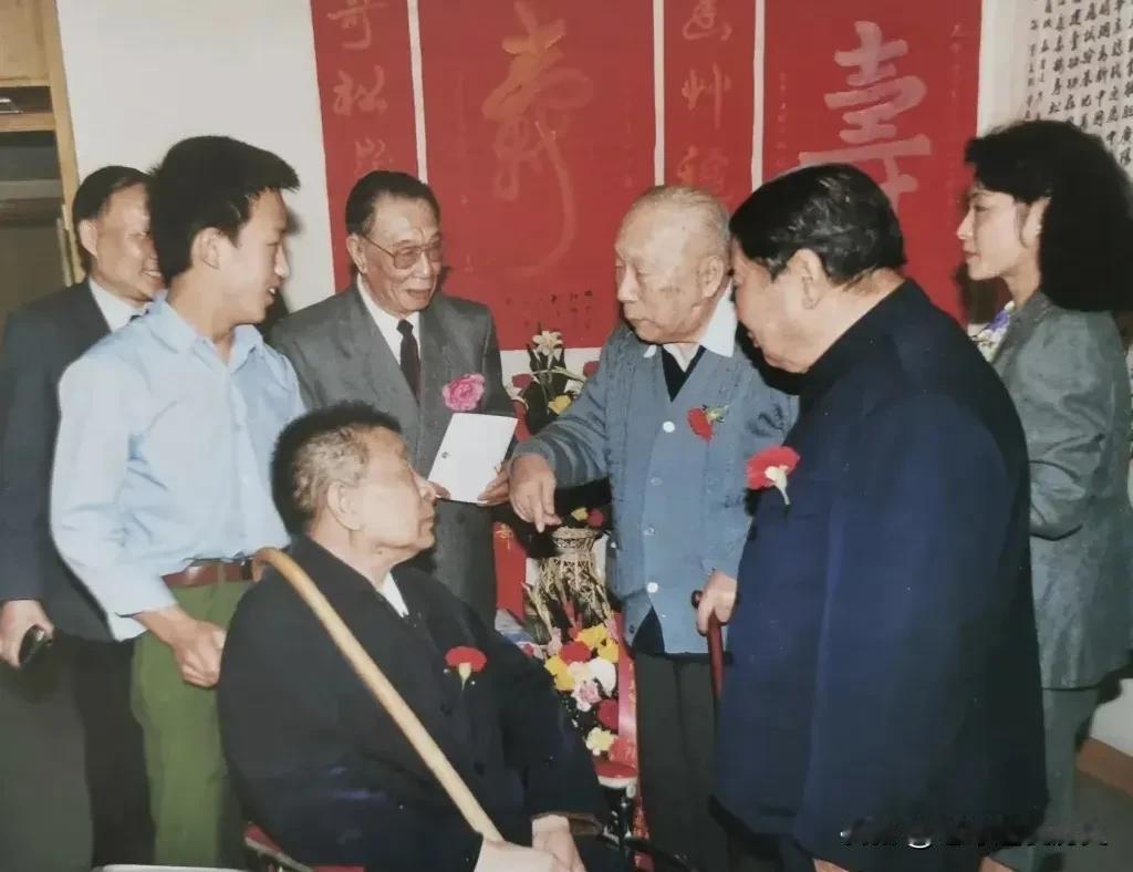 这张老照片定格开国上将陈士榘八十二岁寿诞的珍贵瞬间。
屋内红底寿字条幅高悬，鲜花