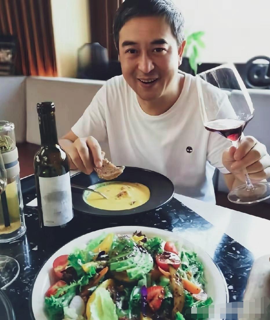 张嘉译，简约白体恤，一只手举着盛有红酒的高脚杯，另一只手拿着面包片，浓汤，蔬菜沙