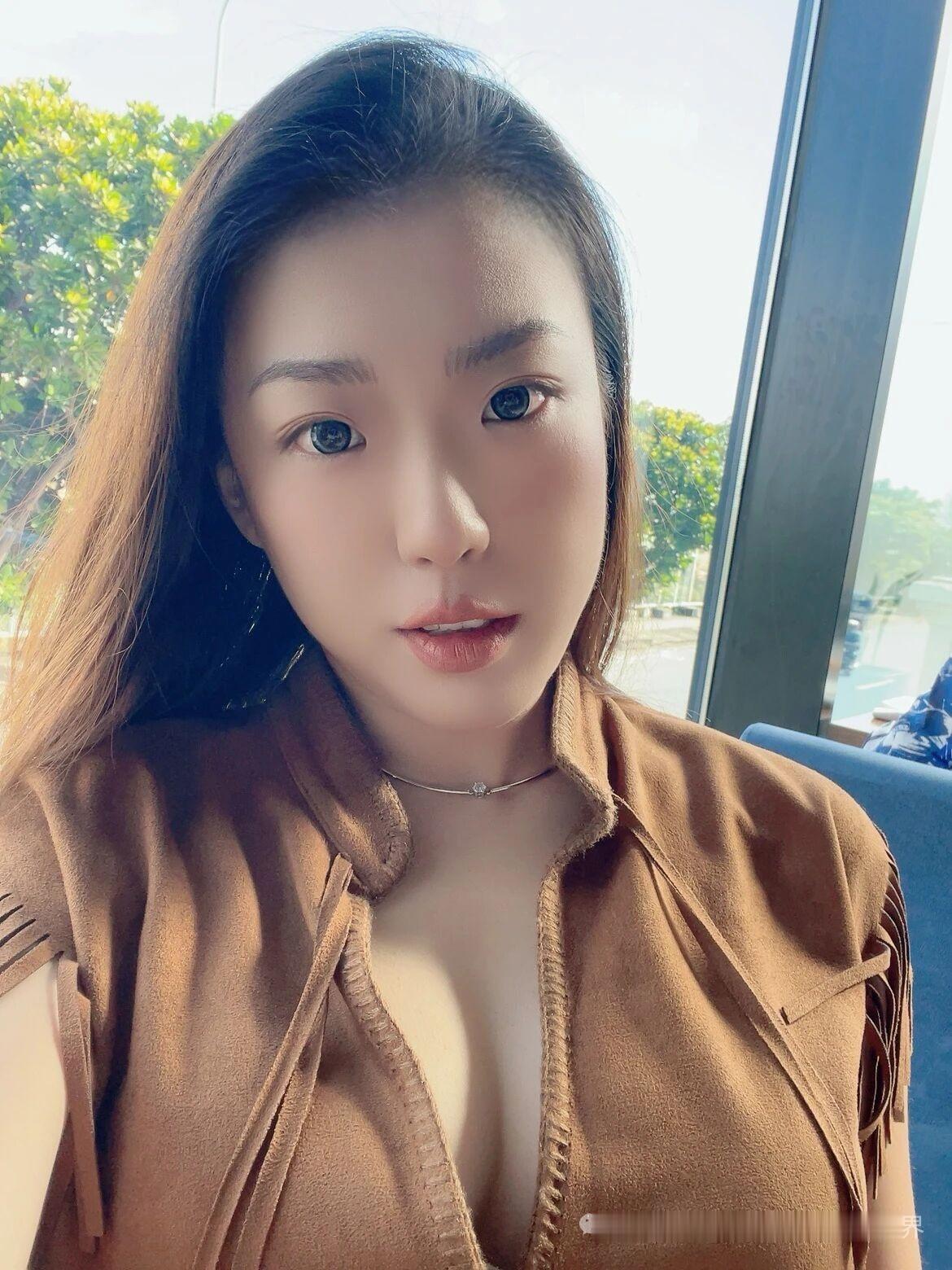 这姑娘穿着棕色外套，坐在窗边。
