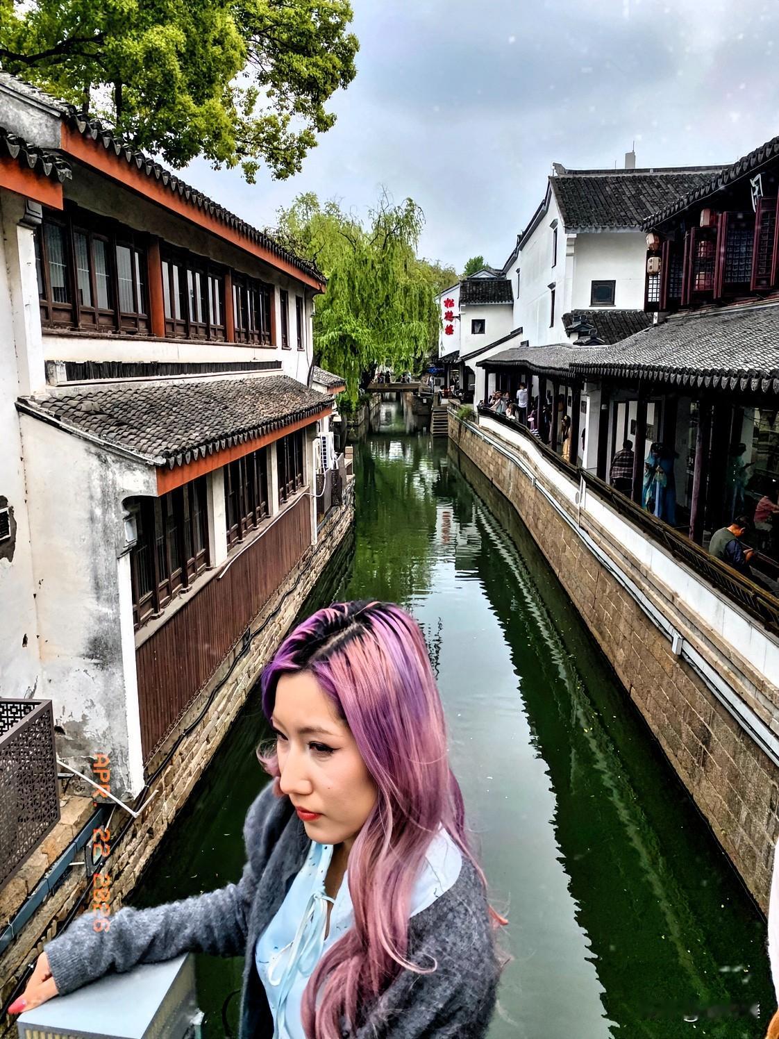 平江河桥坐魔女，
紫红发色时髦衫。
眼神灵动似星闪，
气质超凡映水澜。
桥畔微风