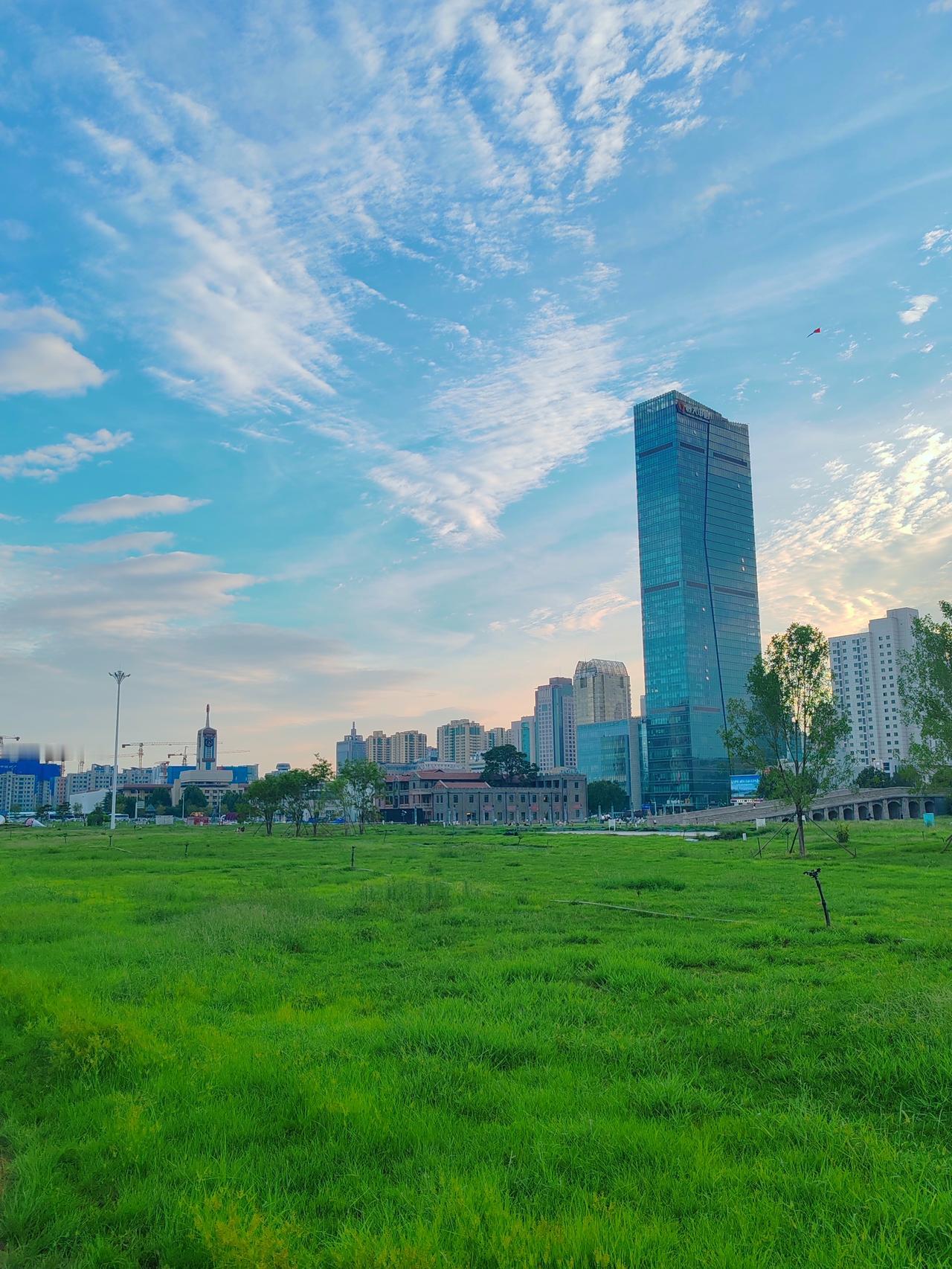拍一张你所在城市最美的景色绿草地，白云朵，高楼耸立向天说，城市美景没的说。