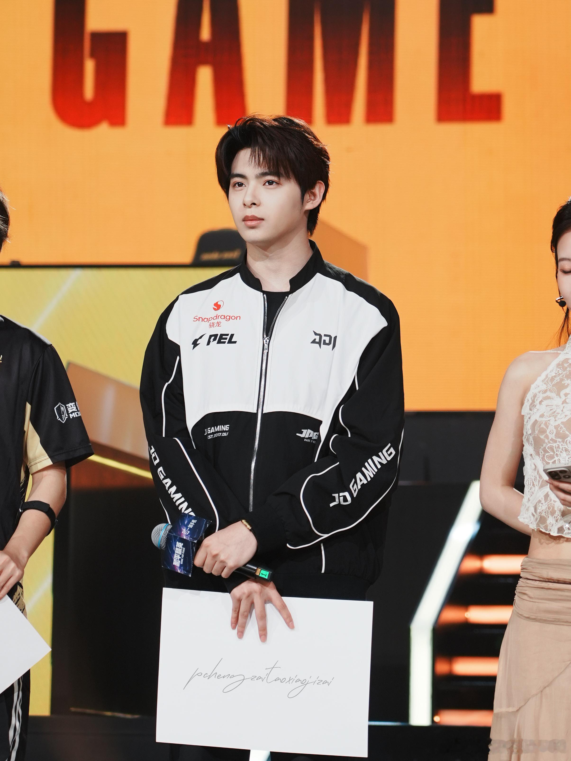 PEL第四周周决赛现场图集。选手身着JDG GAMING队服登台，手持麦克风。背