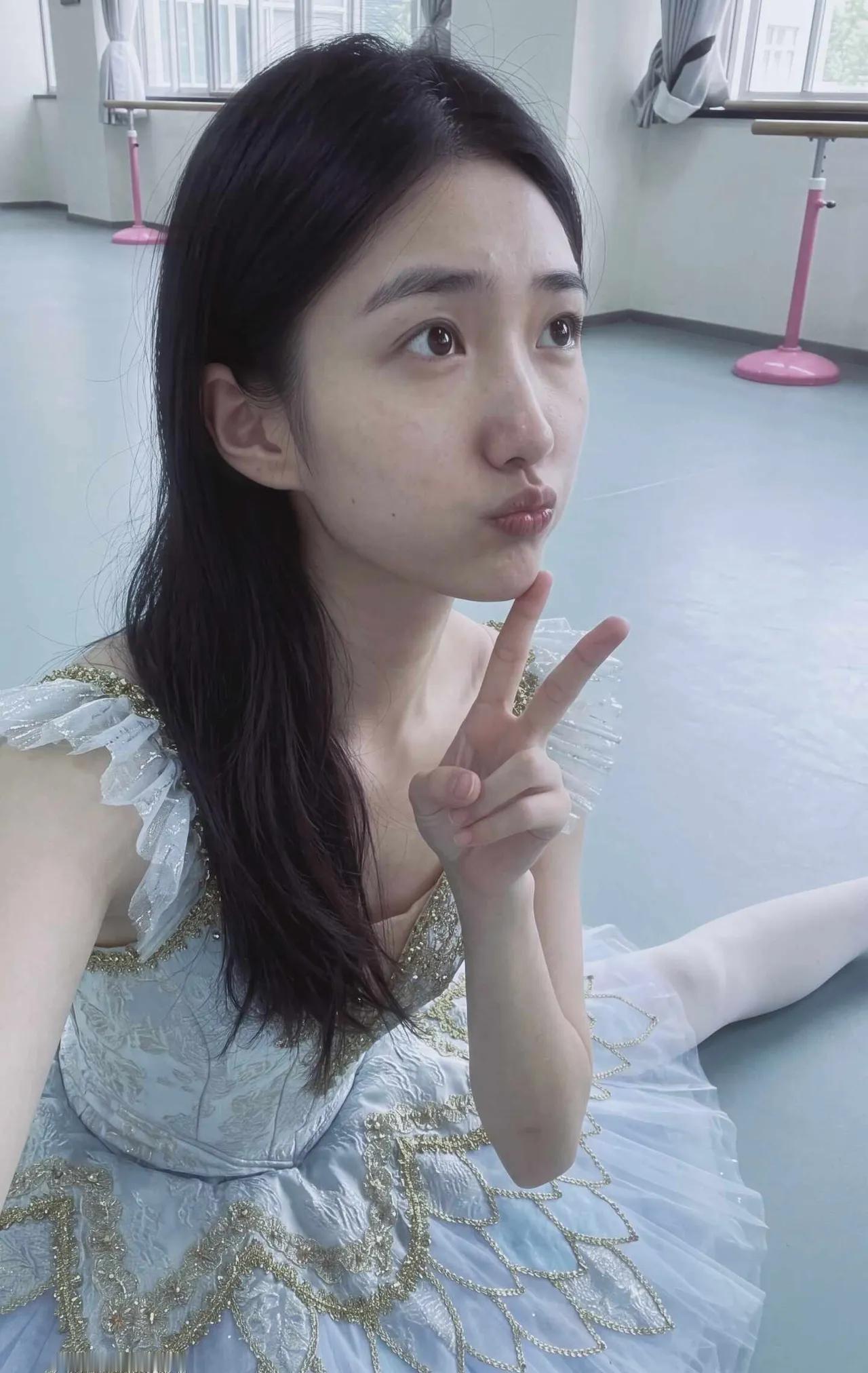 舞蹈女生穿着芭蕾服，在练功房比着V字手势。