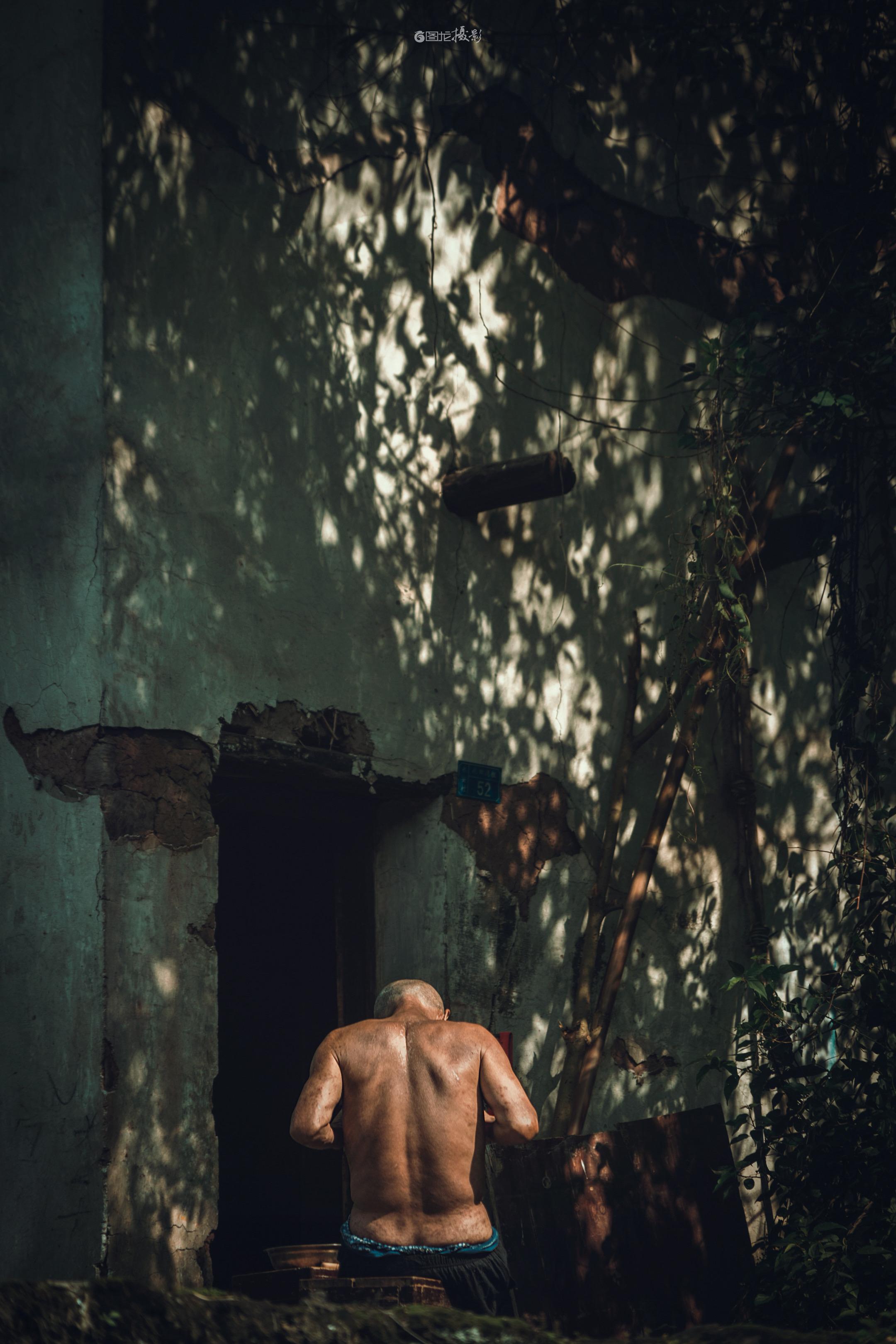 岁月凝于沐时。｜在斑驳的老墙下，树影如细碎的银箔在灰绿墙面上跳跃，一位...