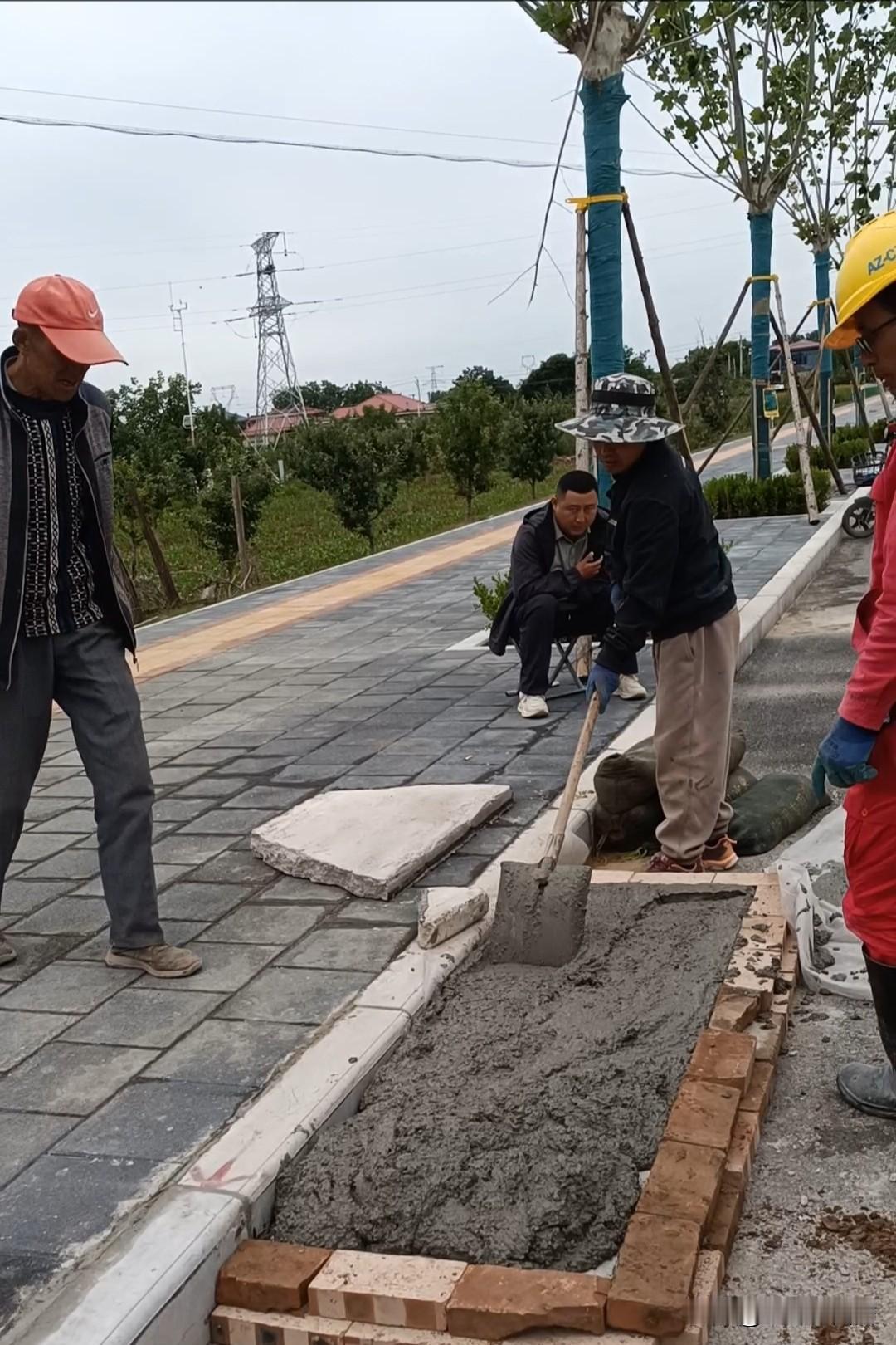 农村新鲜事，阴雨天气，只见几个带安全帽的人起劲的用混泥土填塞路边雨水口，然后用防