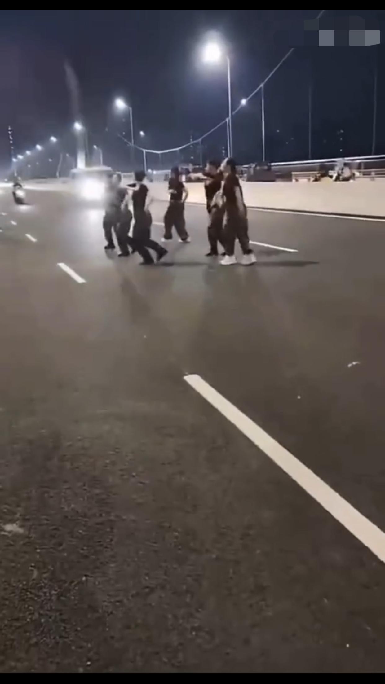 在中国某地的公共机动车道上，一群女子无视来往的车辆，占着车道，在马路中间忘我的跳