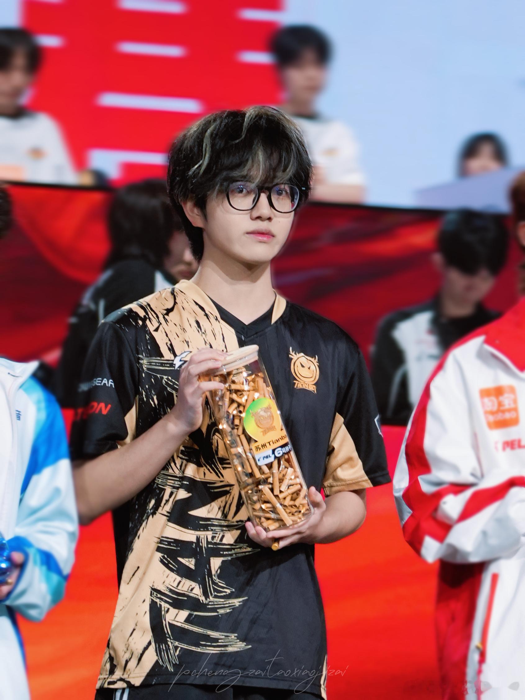 2026PEL夏季赛现场，qzz手持零食罐亮相舞台。黑金队服搭配黑框眼镜，神情专