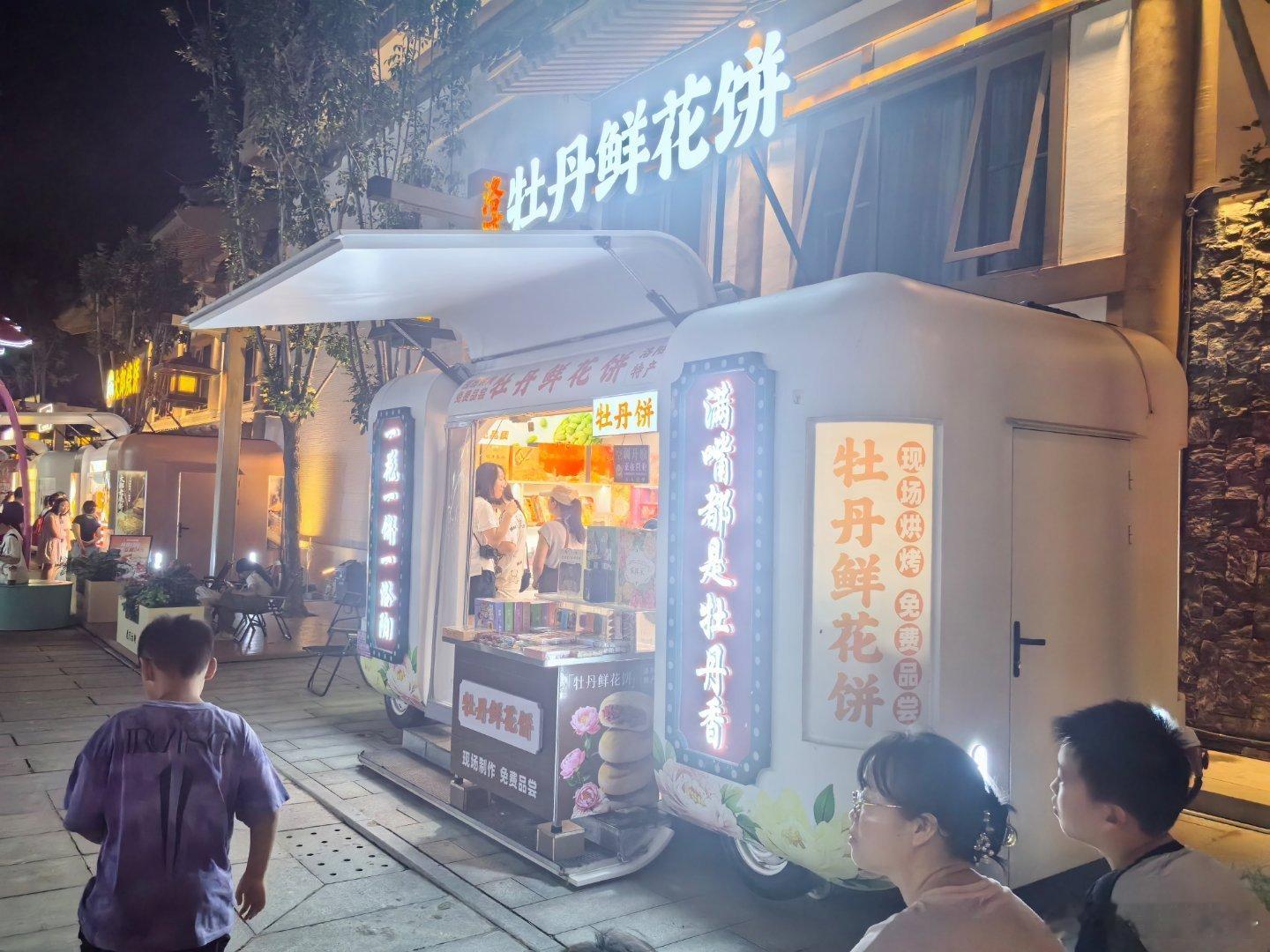 晚风漫过洛阳 龙门古街，成排灯笼把盛唐街巷揉进夜色里。一侧是石窟沉淀千年的龙门石