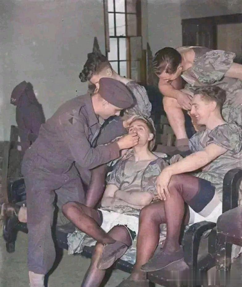 1940年，几名英军男兵身穿长裙丝袜玩起了角色扮演，一旁的战友正在帮他们涂抹口红