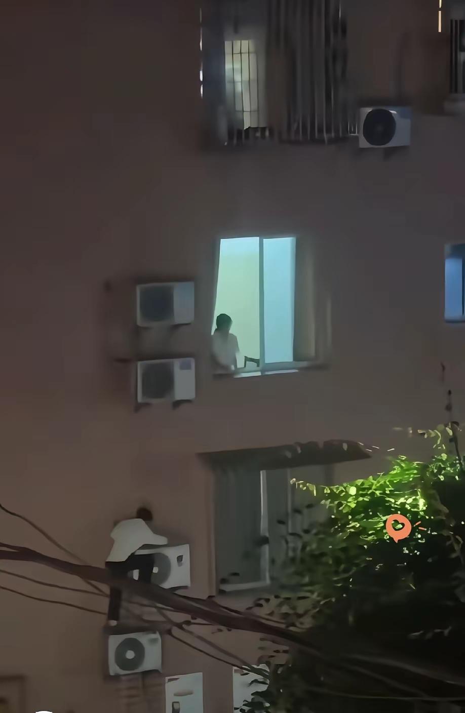 深夜，某地某栋楼外面，一个人爬在外挂空调机外面，向上面攀爬。上面一间房窗户大开，
