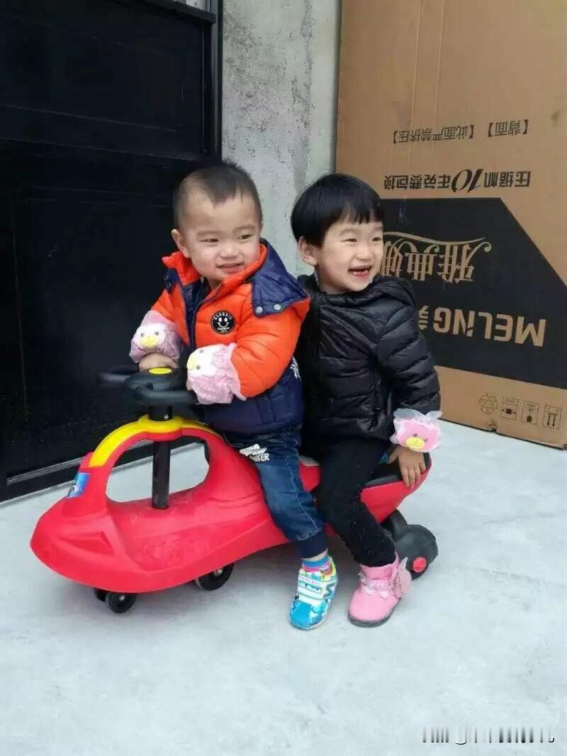 这是一个充满童趣的场景，两个孩子坐在一辆红色的玩具车上，脸上洋溢着天真烂漫的笑容