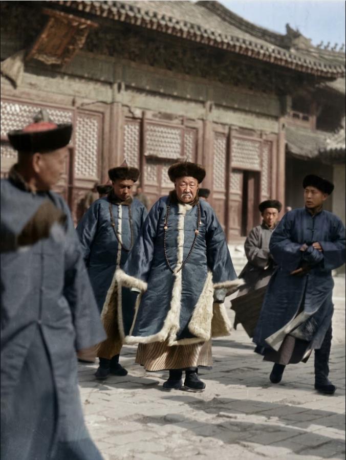 1919年，北京雍和宫，冬季法会期间，一位身着清代官制冬装的官员与随从在庭院中行