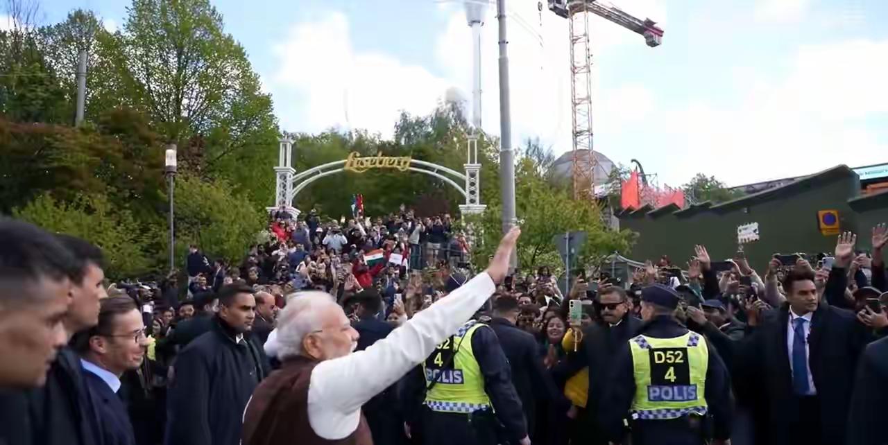 这是莫迪在访问瑞典时的场景，一波人挤在一个小道上，莫迪向人群挥手致意，现场警察维