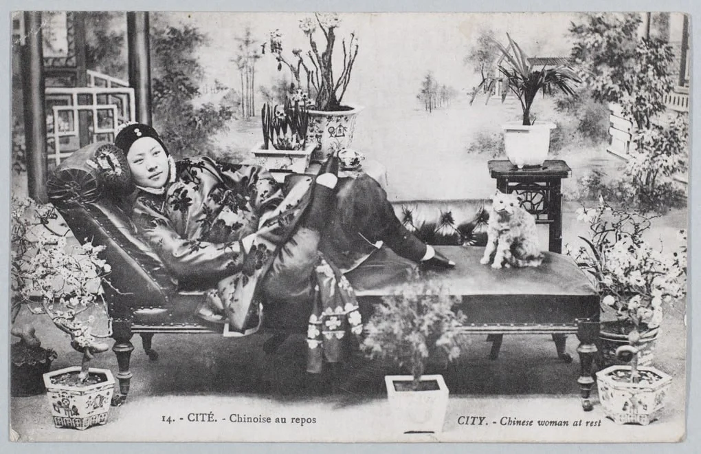1910年，一名女子躺在摄影师工作室的躺椅上，身边有一只毛绒猫。照片背...