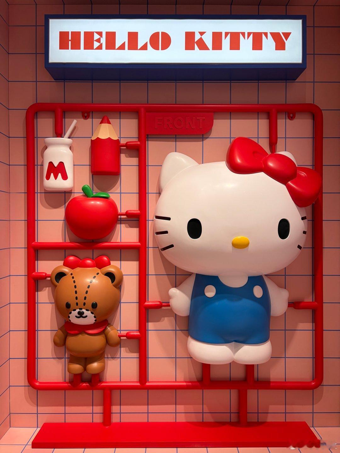 以Hello Kitty为主题的创意商业美陈，将经典IP形象与周边配件（小熊、苹果、牛奶、铅笔）设计成巨型塑料模型“板件”的立体形式。搭配粉色格子背景墙与醒目的“HELLO KITTY”灯箱，整体风格童趣可爱、色彩明快，极具视觉冲击力与互动打卡吸引力。
（空间与色彩，治愈系） ​
