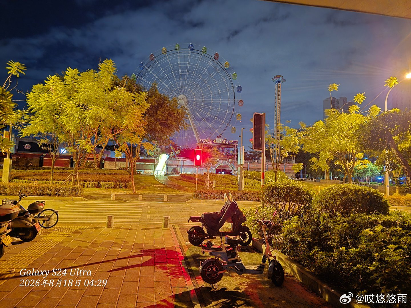 凌晨四点多的游乐园附近，氛围还挺特别的😌 摩天轮在夜色里静静立着，灯光勾勒出它的轮廓，有种安静的美~路上的电动车停得整整齐齐，路灯和树的光影交织，感觉这个时间的街道少了白天的喧嚣，多了份宁静。

说到拍照的设备，我用的是Galaxy S24 Ultra📱 它的夜景拍摄能力真的挺不错的，暗部细节能 ​