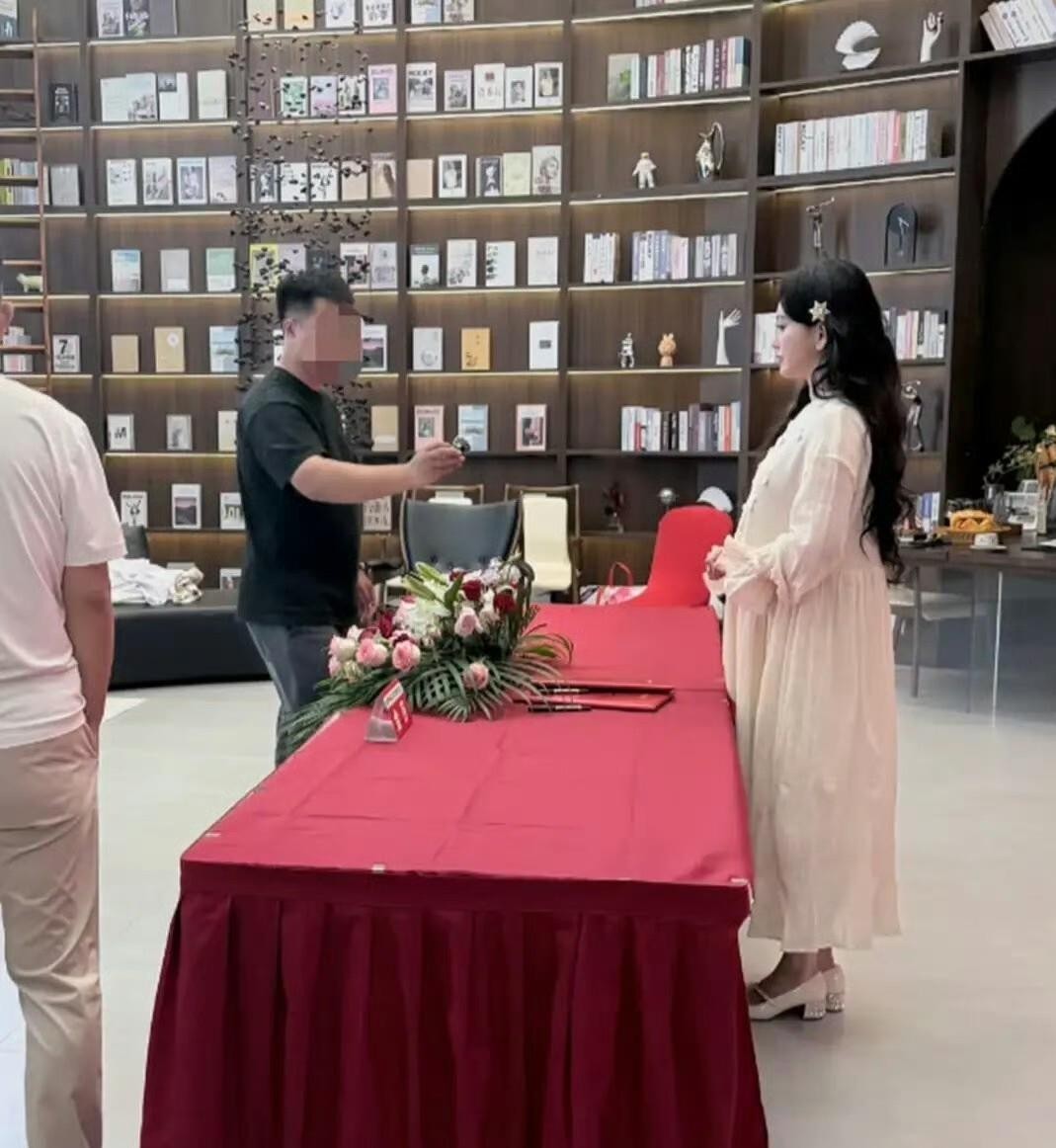 上海那场签约活动的红色背景板前，金莎穿着白色宽松针织裙，长发垂在肩头。 侧身与人合影时，裙料顺着腰腹滑下去，勾勒出一道不容忽视的弧度。 她说话时手掌下意识覆上去，指尖轻轻压着，像护着什么易碎的物事。 低跟鞋踩在地面，步伐比从前慢半拍。 三个月前她才解释过浮肿是因为中俄往返倒时差，那时脸还带着旅途的倦