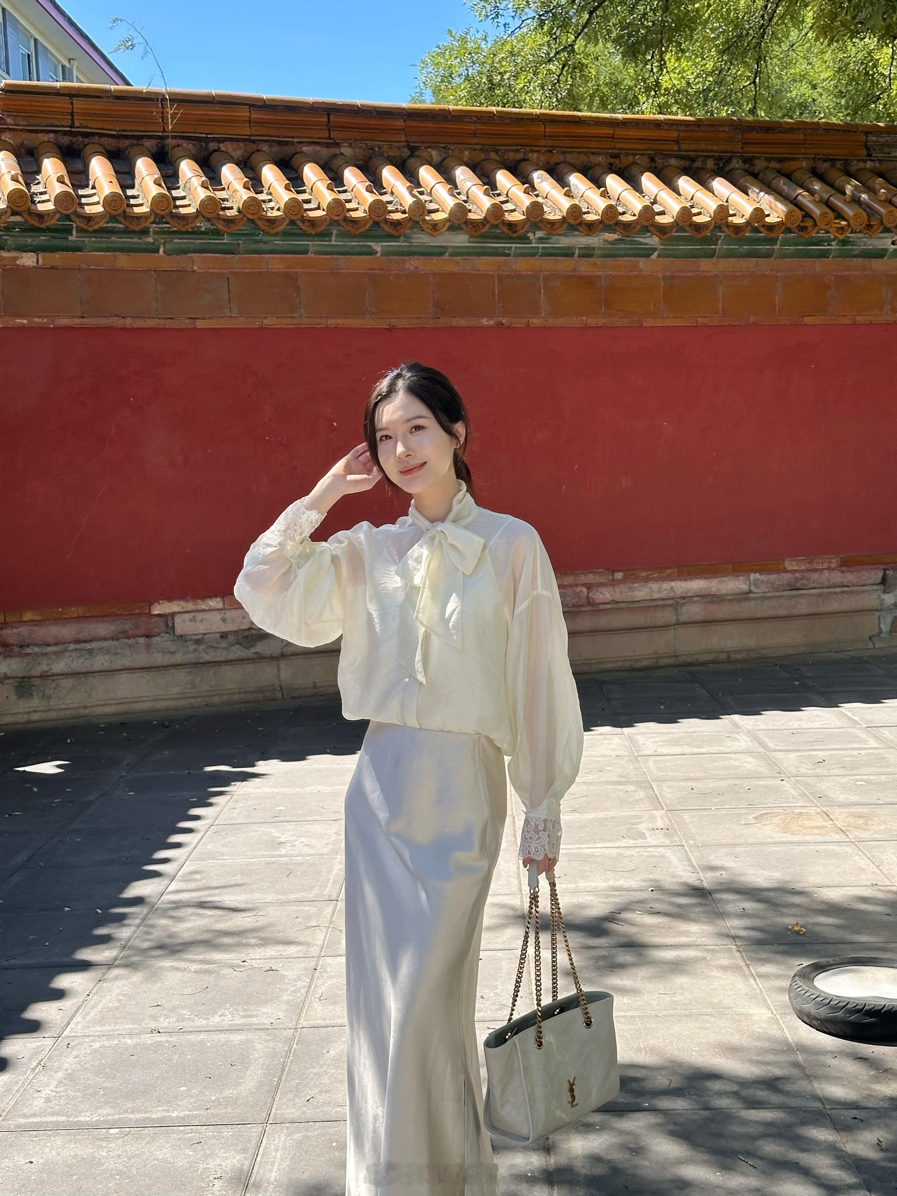 国子监的红墙太有氛围感阳光穿过树叶，落下斑驳树影一墙朱红，衬得一身浅色系格外温柔 选了一套干净的米白套装蝴蝶结衬衫+垂感半裙柔和又自带东方松弛感不用刻意摆动作，走走停停秋天的阳光落在身上，岁月静好 ​​​
