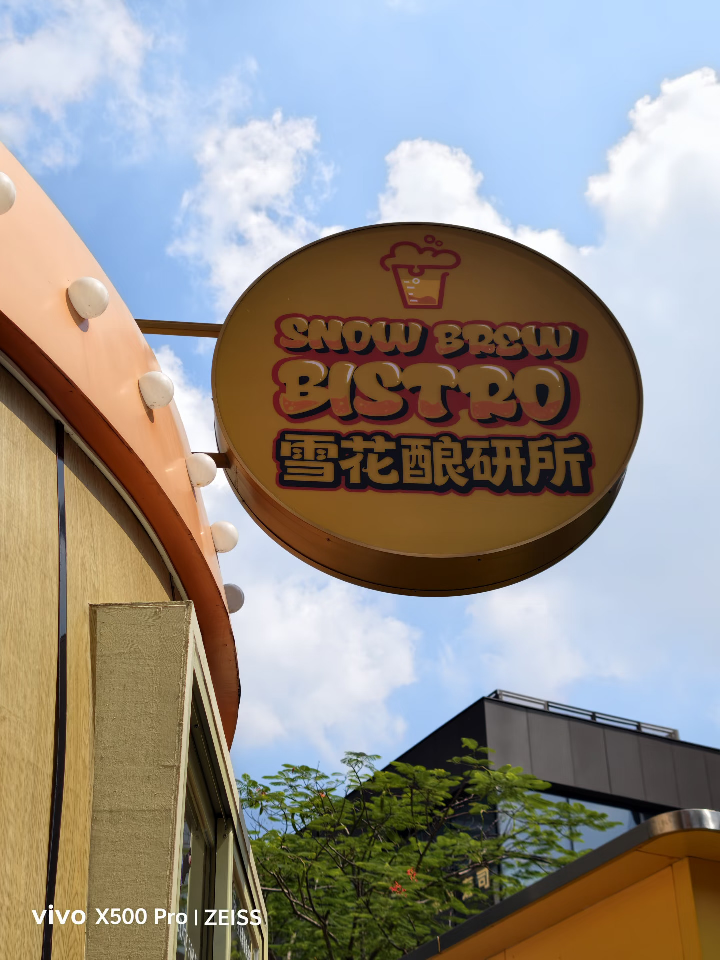 📸 2倍主摄实拍对决！vivo、小米、苹果谁更能打？
这次没找什么复杂场景，就在路边抬头拍了块商家招牌，画面里有蓝天白云、建筑外墙，还有招牌上的文字。看起来很普通，但这种仰拍场景还挺考验手机的，天空和墙面亮度不同，既要看招牌细节，也要看整体色彩和明暗表现！
💙 vivo X500 Pro
三张放一起，我个人第一眼最喜欢 vivo！蓝天看着清爽自然，白云的层次也保留得不错，不会整个天空蓝得发闷。建筑外墙的颜色比较舒服，亮部没有特别刺眼，暗部也没有糊成一片。再看招牌，文字边缘清楚，细节交代得比较到位，放大看也有不错的观感。最关键的是，天空、墙面和招牌这几个部分没有谁特别抢戏，整体看起来很协调。
🔴 小米18 Pro
小米这张的色彩观感更鲜明一些，乍一看挺讨喜，但我个人觉得建筑外墙的明暗层次没那么舒服，部分区域显得有些沉，和蓝天放在一起时，画面的通透感稍微差了一点。整体风格比较浓郁，但不是我最喜欢的方向。
🍎 iPhone 18 Pro
苹果还是熟悉的风格，画面比较克制，整体看着...